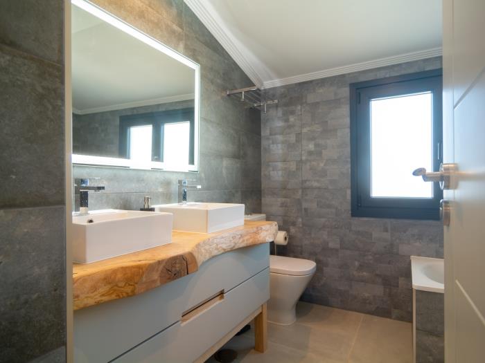 En suite bathroom is equipped with a walk in shower with rain head, a sink, mirror and window