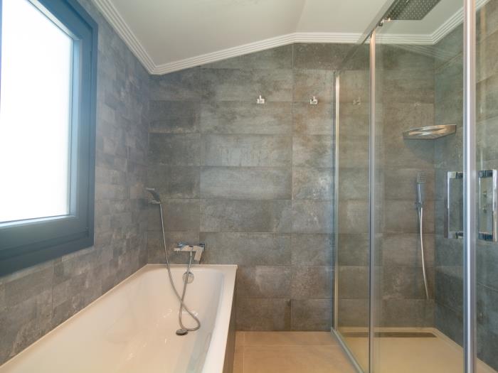 En suite bathroom has a bathtub, a walk in shower, windows, double sink on wooden stand
