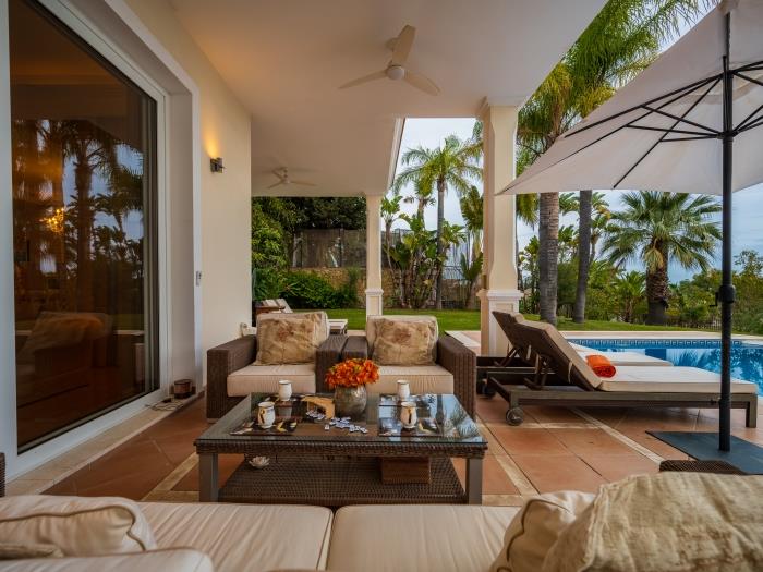 Sitting area with comfortable sofa and armchairs, umbrellas and sun loungers by the heated pool